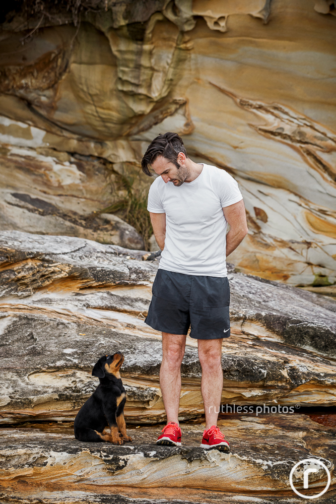 cute rottweiler puppy sitting on rocks looking up at male owner