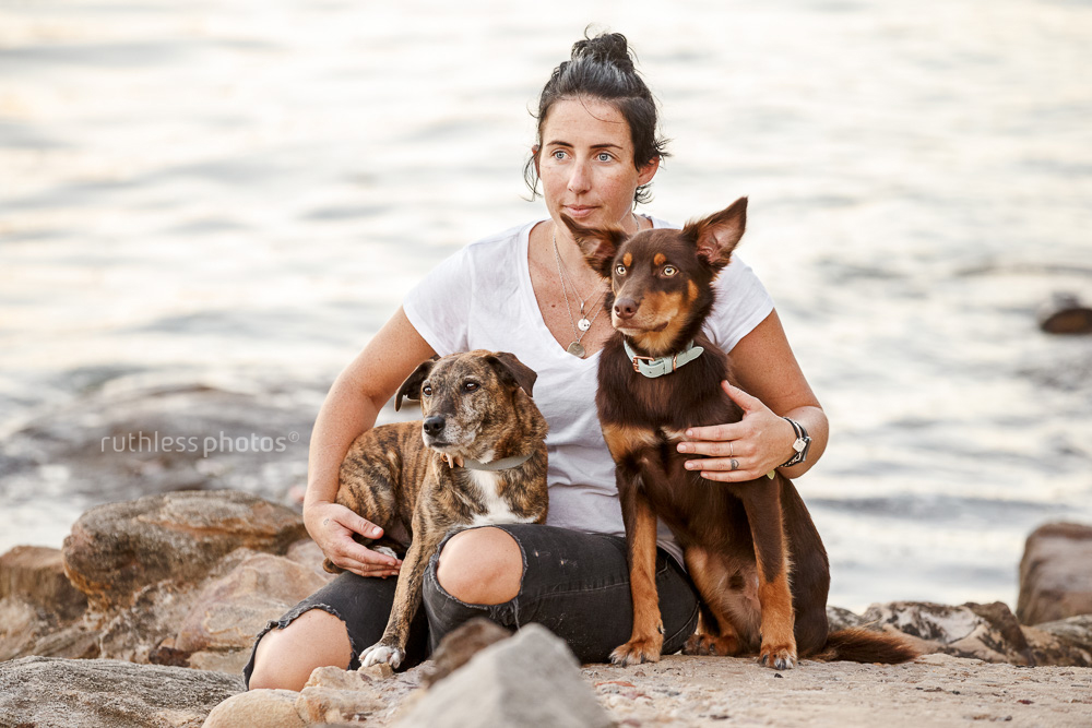 female owner with two dogs sitting beside water looking into distance